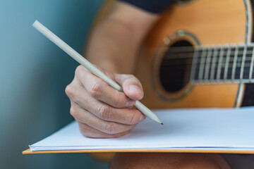 Close-up of a songwriter's hand writing lyrics with a guitar in the background..