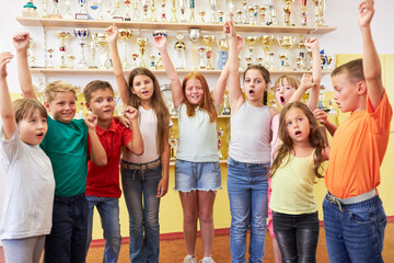 Kids cheering in front of trophy shelf at school