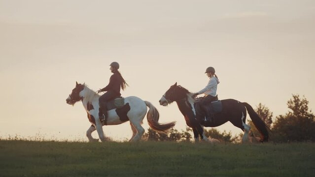 Young women riding horses during golden sunset. Enjoying countryside with horseback riding. Slowmotion shot. 