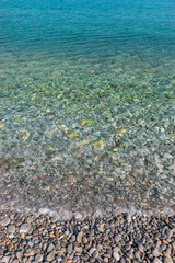 Turquoise calm sea with gray pebbles. Nature background.