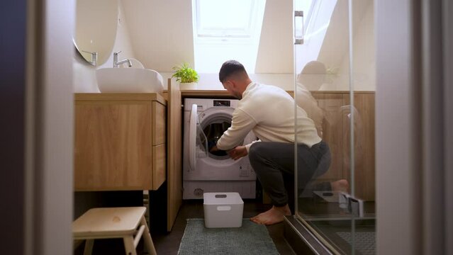 Young man loading clothes into washing machine in bathroom