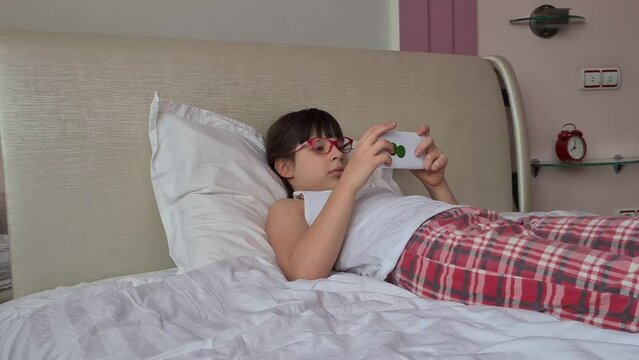 Girl plays games on her phone lying in bed. Gadgets in the child's bed before bedtime