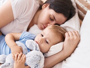 Mother and son sleeping on bed hugging doll at bedroom