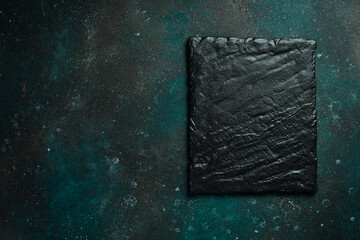 Square slate black plate. On a dark green-turquoise background. Free space for text.