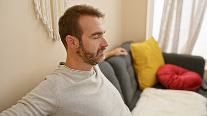 A middle-aged man with a beard relaxes in a cozy living room setting, exemplifying a casual, serene...