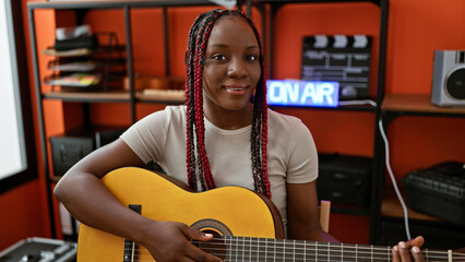 Smiling african american woman plays a classic melody on her guitar indoor. exceptional musician...