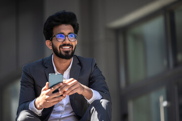 Dark-haired hindu man sitting on the steps with a phone in hands