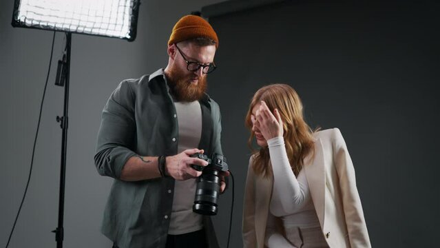 Professional photographer showing pictures to beautiful model during fashion shoot in photo studio