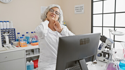 Mature woman scientist experiencing neck pain while working in laboratory