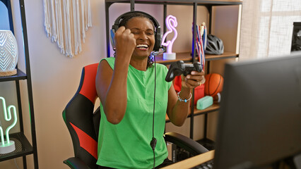 African american woman celebrating in a gaming room with neon lights, computer, and controller