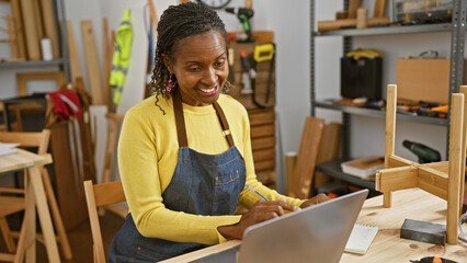 African american woman using a laptop in a carpentry workshop surrounded by woodworking tools