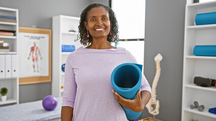 African american woman holding yoga mat in rehabilitation clinic interior
