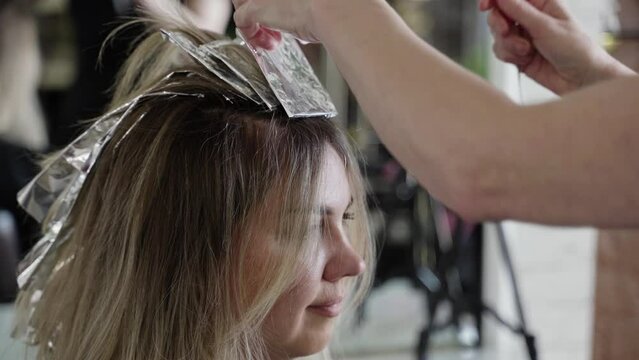 The woman is receiving a trendy hair coloring treatment at the beauty salon, where the hairdresser delicately paints on the color and wraps them in foil for a modern look.