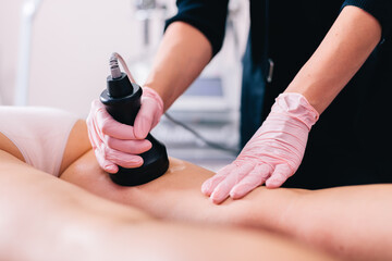 Woman, a beautician doing cavitation liposuction cosmetic procedure on her client thigh in a beauty salon. Fat reduction - obrazy, fototapety, plakaty