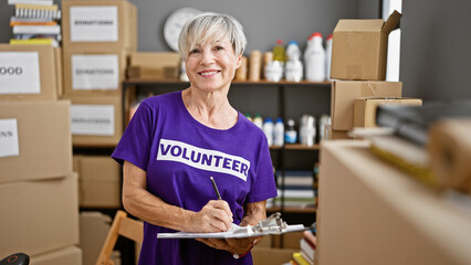 Mature woman volunteering at a warehouse takes notes among labeled boxes indoors.
