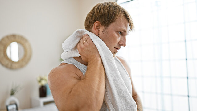 A young blond man with a beard drying off with a towel in a bright home interior. - Powered by Adobe