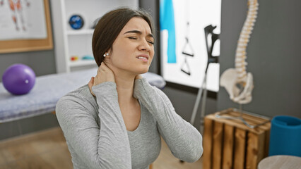 Hispanic woman experiencing neck pain in a physical therapy clinic's interior.