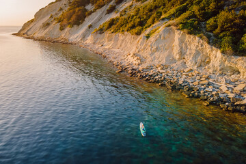 Traveling on stand up paddle board at sea with scenic Mediterranean landscape. Aerial view