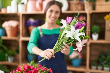 Young beautiful hispanic woman florist holding bouquet of flowers at flower shop