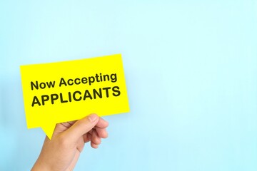 Human hand holding yellow speech bubble with written phrase Now Accepting Applicants. Recruitment and job hiring concept.