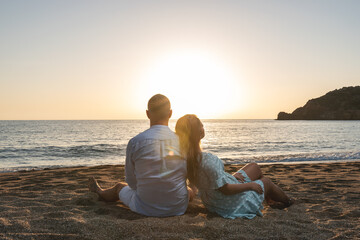 Happy couple in love, is seating on the beach during sunset or sunrise. Summer vacations.