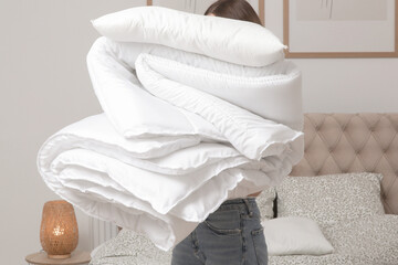 Woman holding pile of soft white folded duvet and pillows at home in her bedroom, cozy domestic lifestyle, housewife cleaning, tidying up bedroom, housework chores concept.	