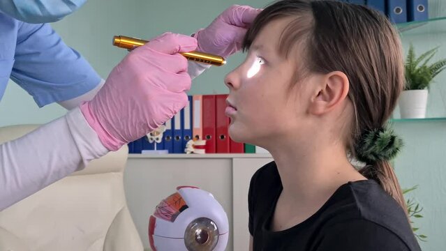 An ophthalmologist carefully examines a young girls eyes with a flashlight, checking for abnormalities