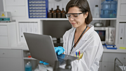 Dedicated young hispanic woman scientist, focused at her laptop in the lab, part of a new wave of...