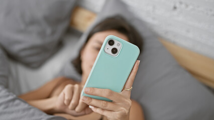 Morning bliss, young beautiful hispanic woman relaxing in bedroom, comfortably lying on bed using smartphone, typing messages online