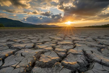 Fotobehang Sunbeams pierce through clouds over a parched earth, where deep cracks in the dry soil create a dramatic testament to the severity of drought conditions against a backdrop of distant mountains. © Sunshine