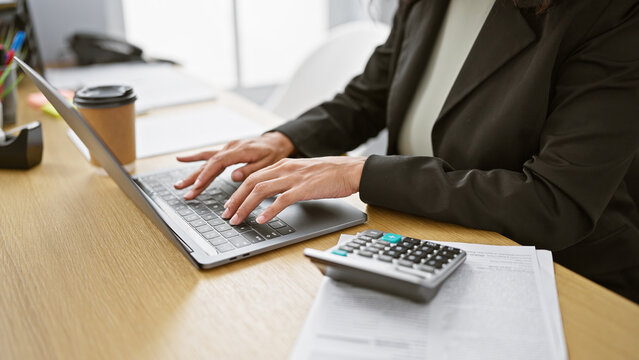 Hardworking woman boss managing business accounts indoors, working with laptop and calculator at office desk