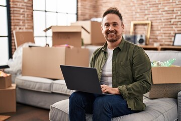 Young caucasian man using laptop sitting on sofa at new home