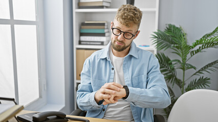 A young caucasian man with a beard and blue eyes, wearing glasses, checks the time in a modern...