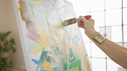 Senior woman artist's hands gracefully drawing on canvas in art studio, a lesson in creativity for...