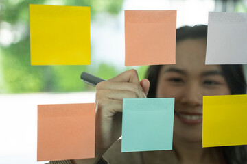Young Asian businesswoman at new ideas on glass wall with adhesive notes.