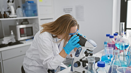 Determined young blonde scientist woman fully engrossed, working meticulously with microscope in...