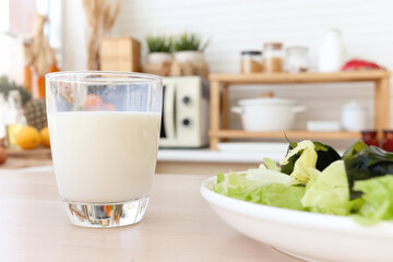 Glass of fresh milk and seaweed salad plate on wooden table with blur modern cozy kitchen...