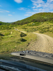 Off-road track or off-road piste over a gravel road with curves in mountains with green meadows and...