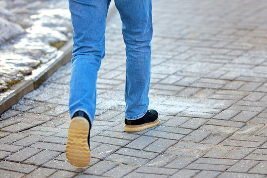 Man walking on sidewalk covered with rock salt and sand, prevent slipping. Salt sprinkled on paving slabs, prevention of pedestrian injury. Treatment of sidewalk with salt in winter. Selective focus