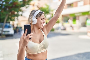 Young blonde woman listening to music and dancing at street