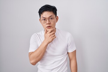 Fototapeta na wymiar Young asian man standing over white background looking fascinated with disbelief, surprise and amazed expression with hands on chin