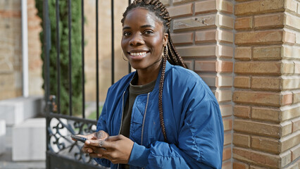 African american woman with braids smiling while using smartphone on urban street