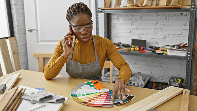 African american woman in a workshop talking on the phone while selecting paint colors from a swatch.