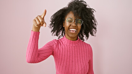 A joyful african american woman wearing glasses giving a thumbs-up in a pink room.
