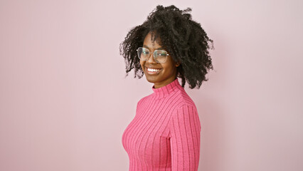 African american woman with glasses poses indoors against a pink background, exuding confidence and...