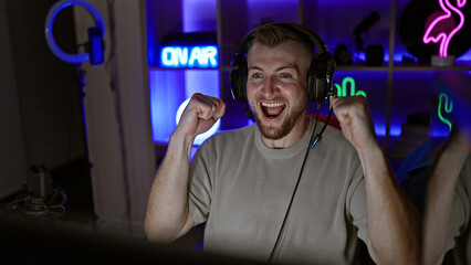 Excited caucasian man with headphones in a dark gaming room celebrating a victory at night.