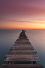 vertical sunrise seascape with an old wooden dock leading out into the calm ocean waters
