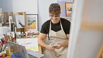 Attractive young hispanic man, an emerging artist, cheerfully engages with technology--laptop and...