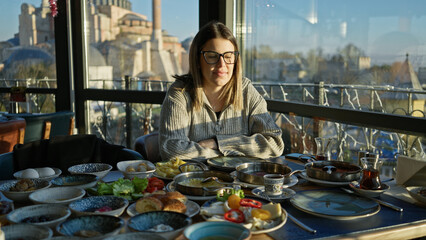 A young woman enjoys breakfast in a restaurant with a view of the hagia sophia in istanbul, turkey