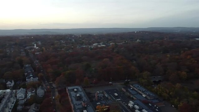 Aerial drone footage over the East Rock neighborhood in New Haven, Connecticut, capturing residential streets, tree-lined blocks, and a clear view of the downtown skyline in the background.
